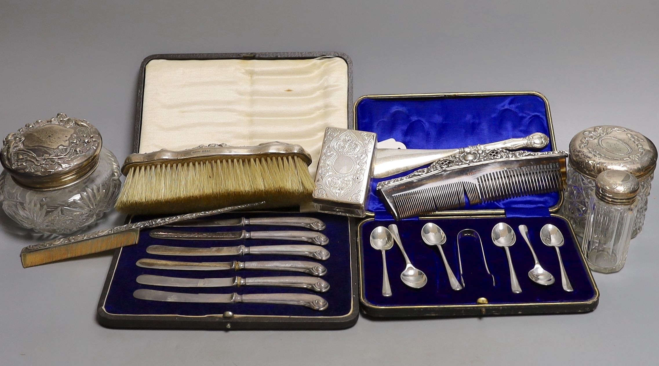 Four assorted silver mounted glass toilet jars, a silver mounted brush, two combs and a shoe horn and two cased sets of cutlery including silver teaspoons with tongs.
